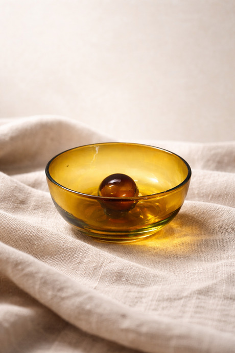 Amber glass bowl with a sphere on a beige fabric background