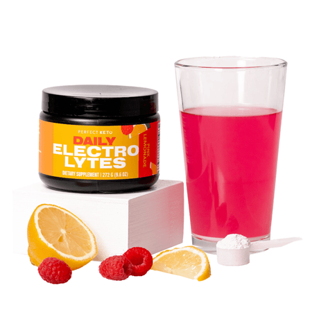 Jar of 'Daily Electrolytes' supplement with a glass of pink liquid, lemon, raspberries, and a scoop on a white background.