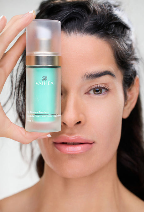Woman holding a skincare product with 'VAIHEA' branding against a neutral background