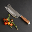 Mezzaluna knife with wooden handle on a dark surface with tomatoes and rosemary.