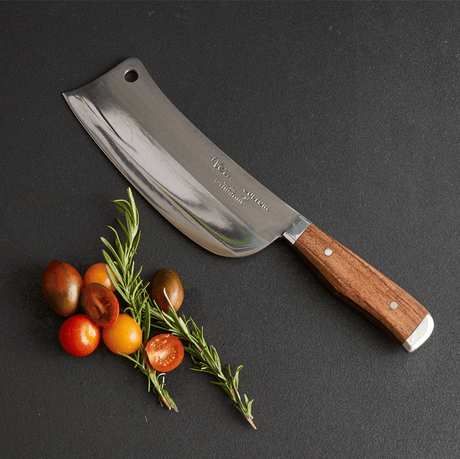 Mezzaluna knife with wooden handle on a dark surface with tomatoes and rosemary.