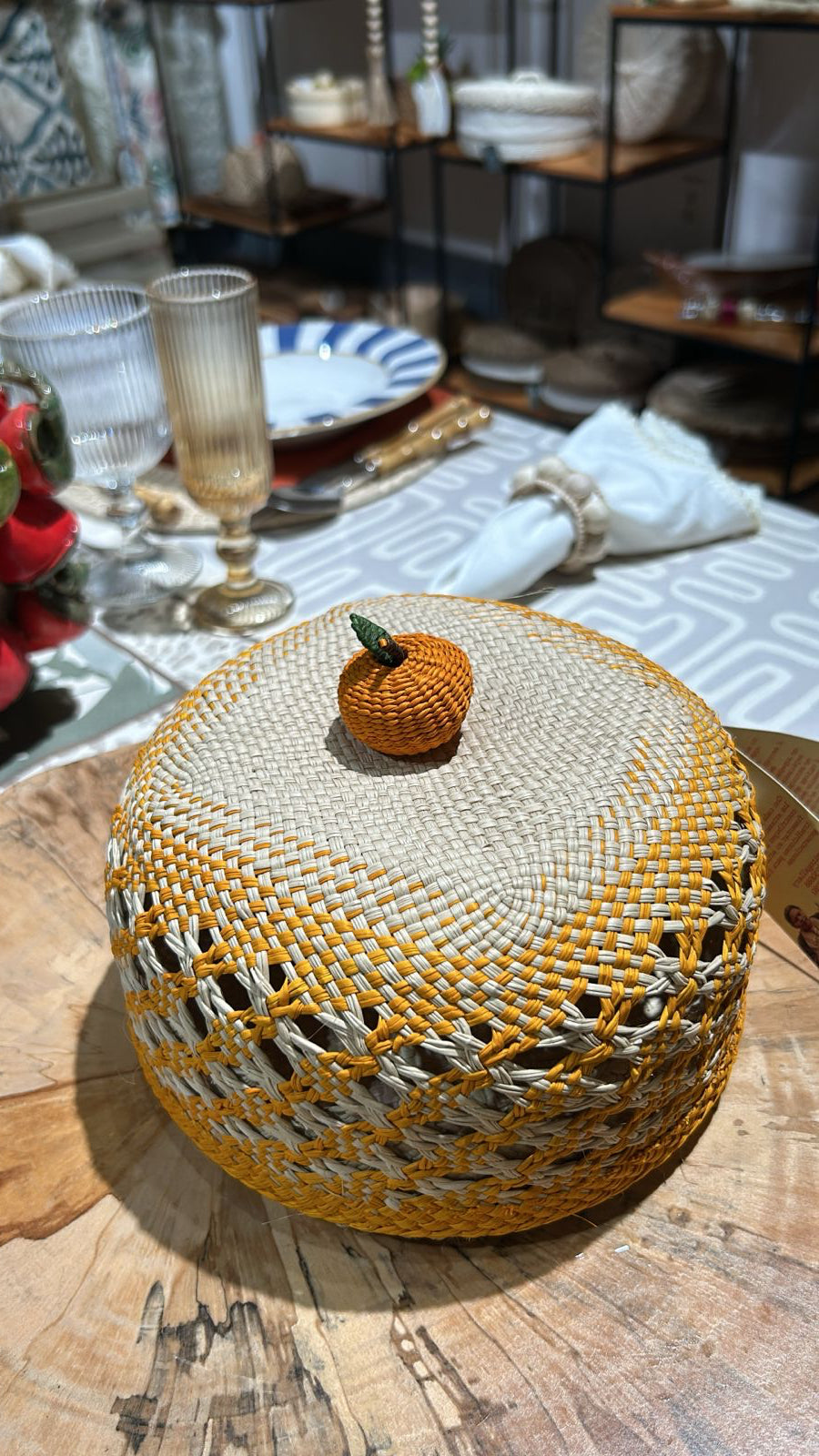 Woven bread basket  with a small pumpkin decoration on a table with a patterned tablecloth.