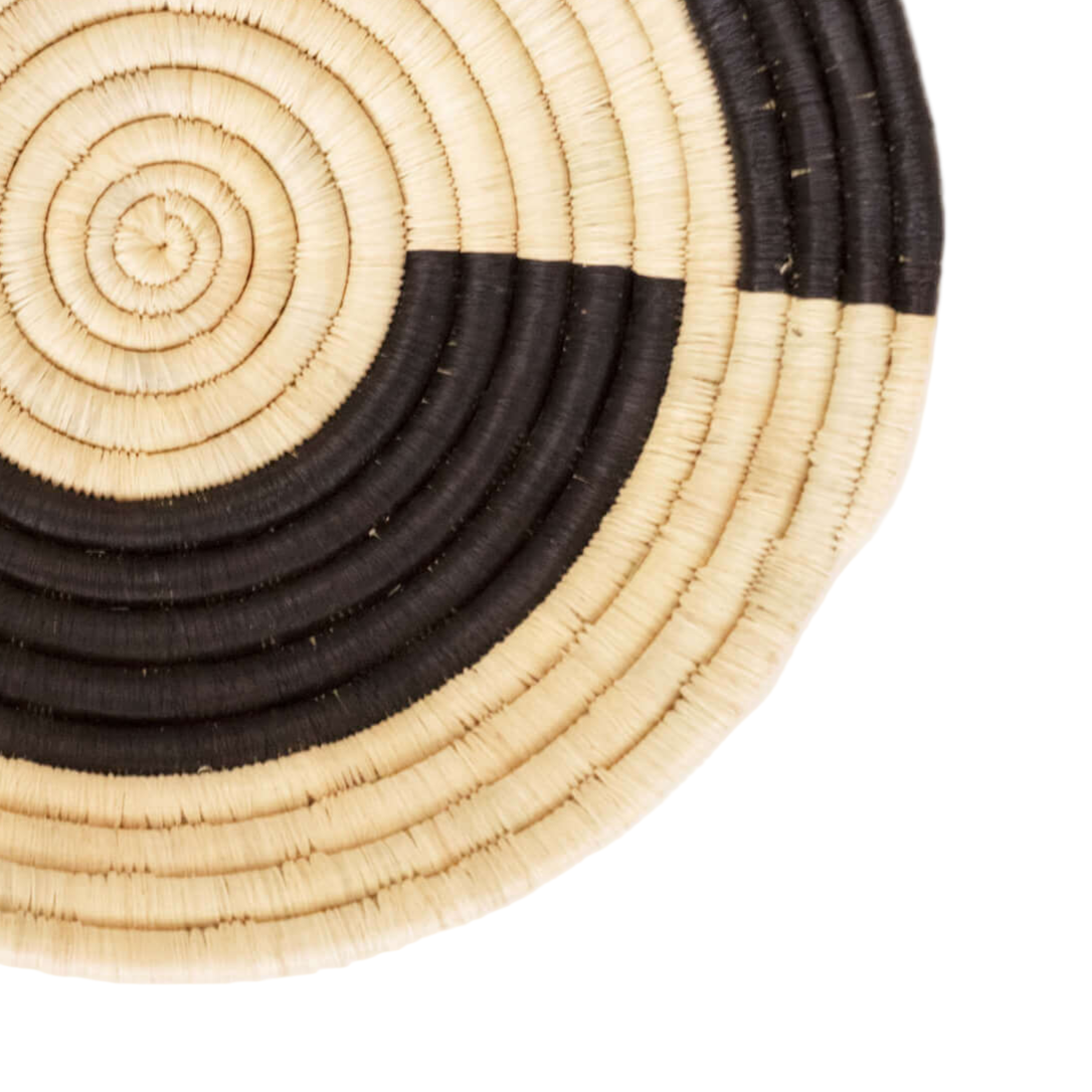 Round woven basket with black and beige concentric circles on a white background