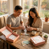Two people sitting at a table with craft materials and coffee, smiling.