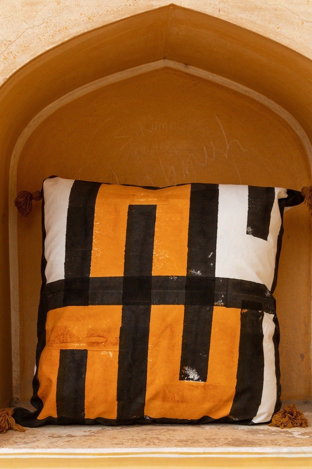 Decorative pillow with black and orange pattern on a beige wall background