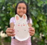 Child holding a ceramic bunny plate with a blurred green background