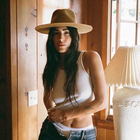 Woman wearing a beige hat indoors with wooden walls and a lamp in the background