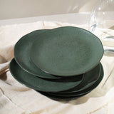 Set of three green ceramic plates stacked on a light fabric surface