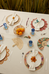 Decorative table setting with colorful plates, napkins, and cutlery on a white tablecloth.