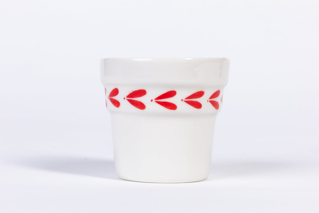 White ceramic espresso cup with red leaf pattern on a white background