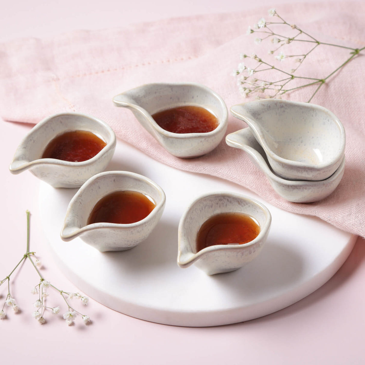 Set of ceramic condiment bowls with a liquid inside on a pink surface with decorative elements.