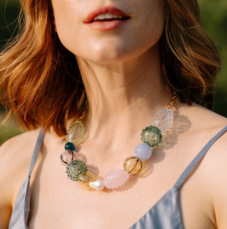 Close-up of a woman wearing a colorful beaded necklace with a blurred natural background