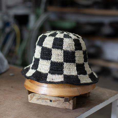 Black and white checkered bucket hat on a wooden block with a blurred background