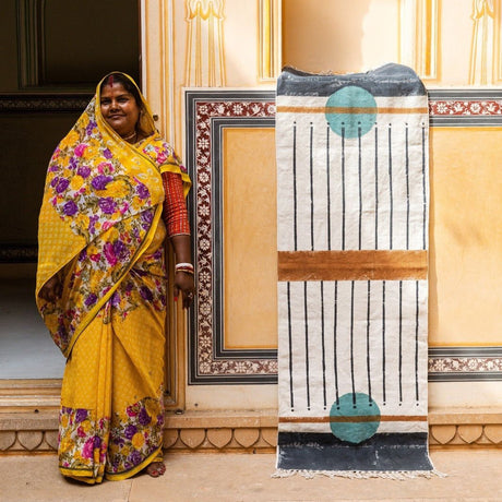 Woman in a yellow saree standing next to a decorative screen with intricate patterns.