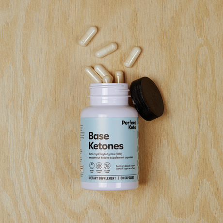 Supplement bottle labeled 'Perfect Keto Base Ketones' with capsules on a wooden surface