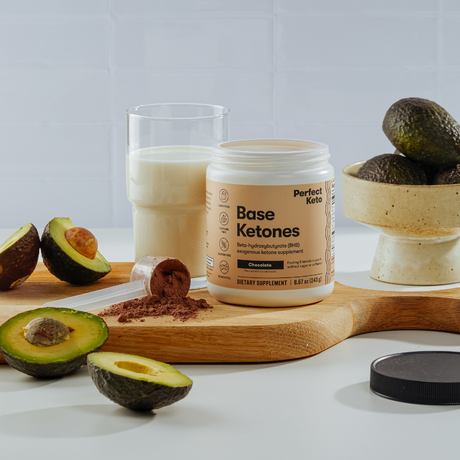 Perfect Keto Base Ketones container with avocados and a glass of milk on a wooden board.