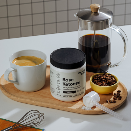 Base Ketones container with a cup of coffee, French press, and coffee beans on a wooden tray.