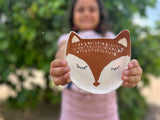 Person holding a ceramic fox plate with a blurred green background