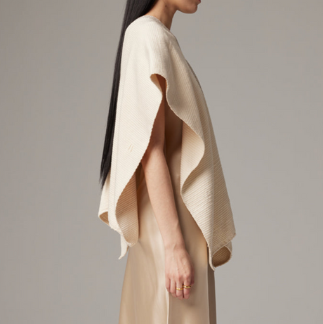 Woman wearing a beige knitted poncho against a plain background