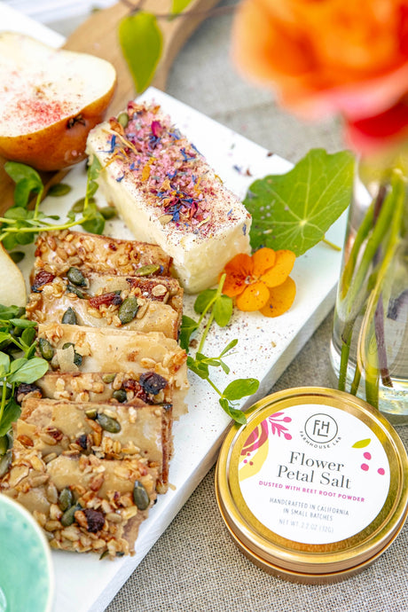 Platter of assorted snacks with a container of Flower Petal Salt on a textured surface.