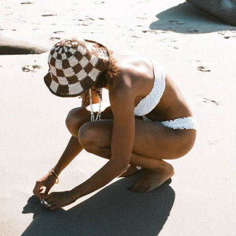 Person in a white bikini and checkered hat on a sandy beach