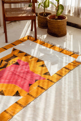 Quilt with geometric pattern on a white floor with plants and a chair in the background