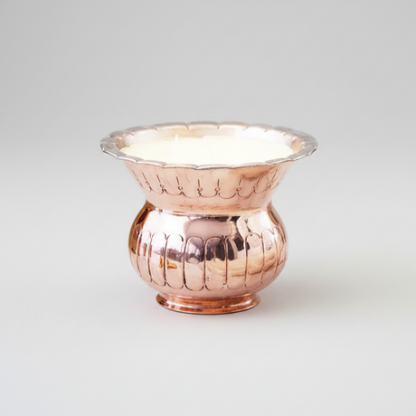 candle in Copper vase with textured design on a white background