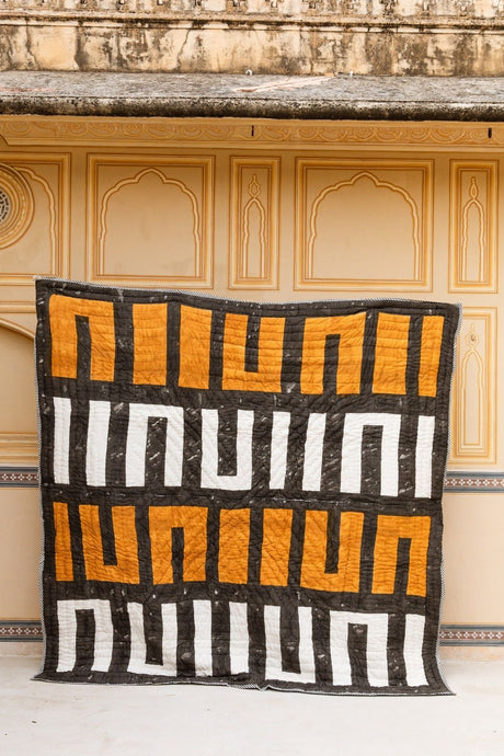 Textile with orange and white patterns draped over a decorative wall.