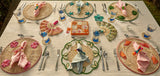 Dining table set with wicker placemats, cutlery, and decorative items outdoors.