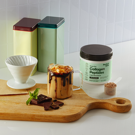Collagen peptides container with a cup of iced coffee and chocolate on a wooden board.