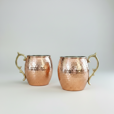 Two copper mugs with gold handles on a light gray background