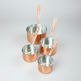 Set of four copper measuring cups with handles on a white background