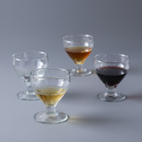 Four small glass cups with different colored liquids on a white background