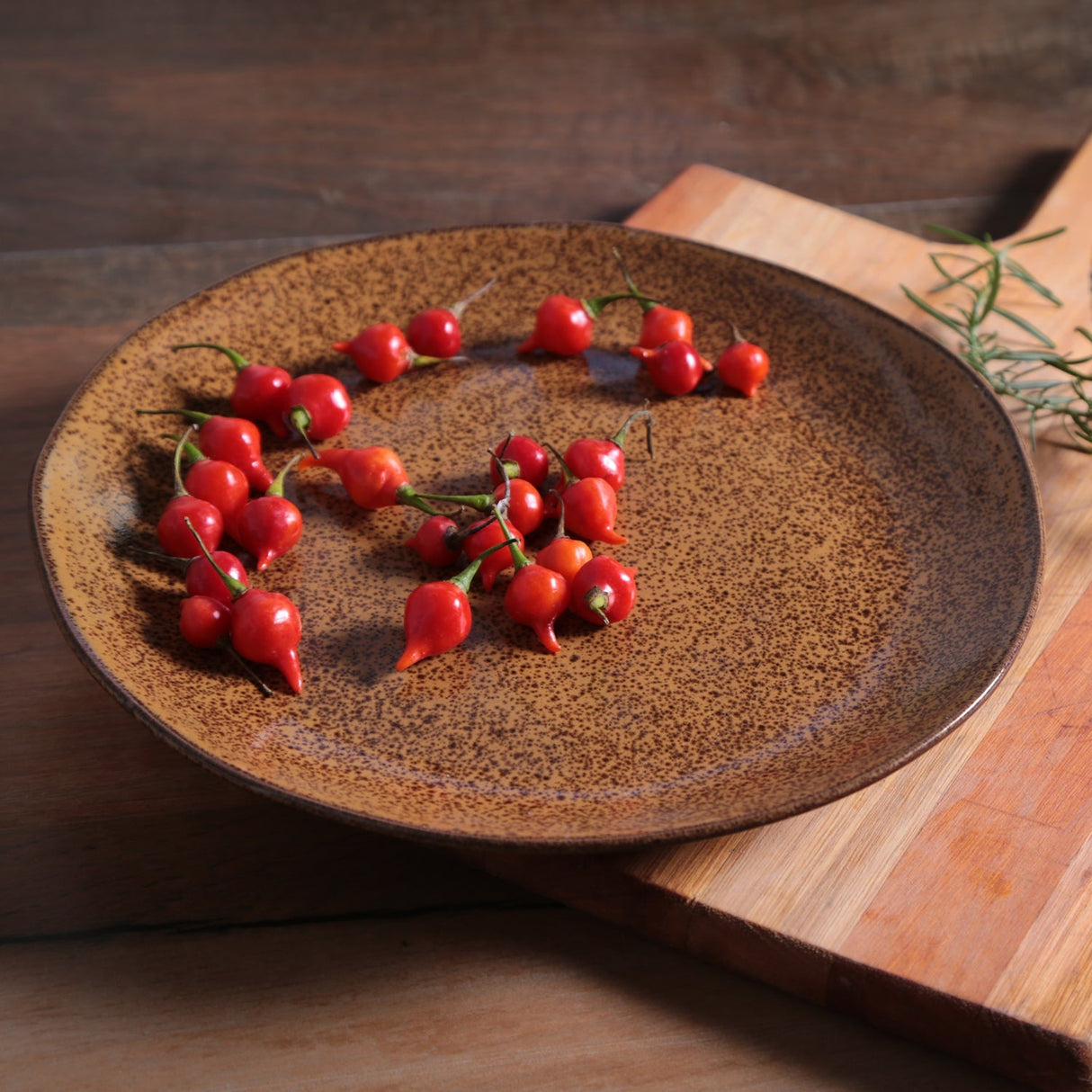 Red chili peppers on a textured ceramic plate with a wooden background