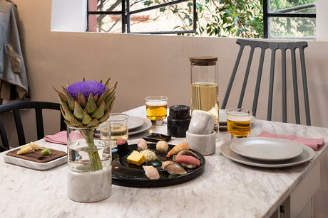 Dining table set with plates, glasses, and a vase with an artichoke on a marble countertop.