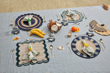 Dining table setup with place mats, cutlery, and food items on a striped tablecloth.