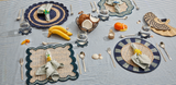 Dining table setting with placemats, cutlery, and decorative items on a striped tablecloth.