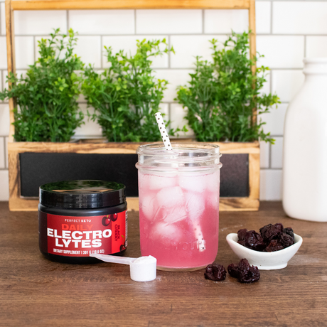 Pink iced drink in a mason jar with a straw, next to a jar labeled 'Electrolytes' on a wooden surface with plants in the background.