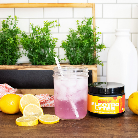 Mason jar with pink iced drink and lemon slices on a wooden surface with 'Daily Electrolytes' container.