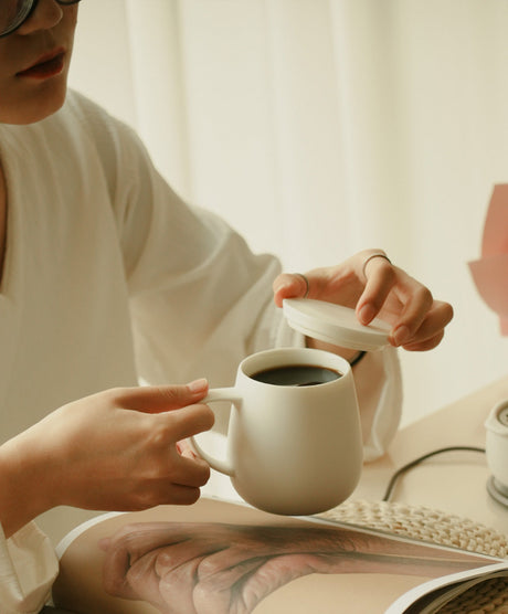 Person holding a white mug with coffee, with another person's hand reaching towards it.