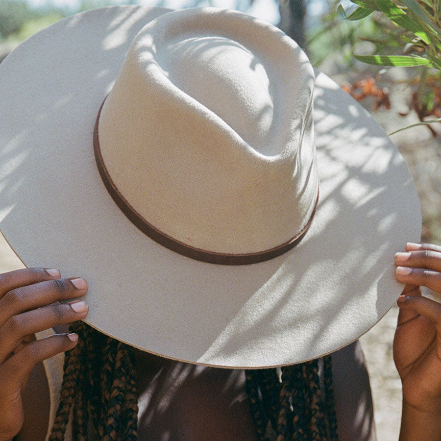 Person holding a beige wide-brimmed hat with a blurred natural background