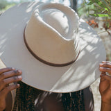 Person holding a beige wide-brimmed hat with a blurred natural background
