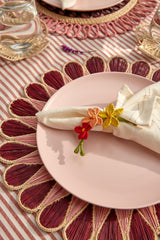 Decorative table setting with pink plates, napkins, and floral napkin rings on a striped tablecloth.