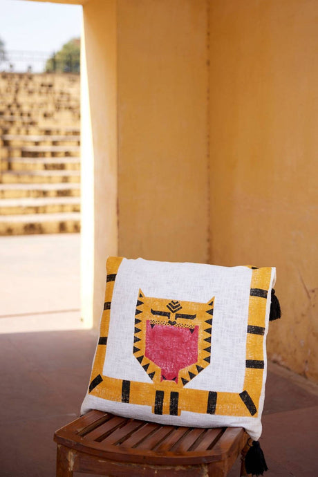 Decorative pillow with a tiger design on a wooden stool against a beige wall.