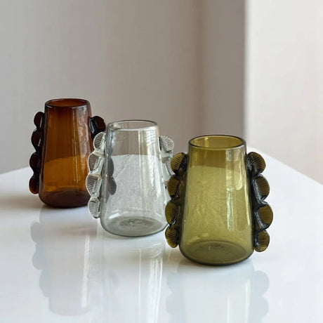 Three glass vases with unique handles on a reflective surface.