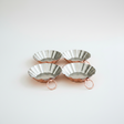 Four metallic tart tins with rose gold stands on a white background