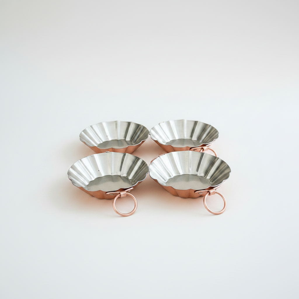 Four metallic tart tins with rose gold stands on a white background