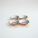 Four metallic tart tins with rose gold stands on a white background
