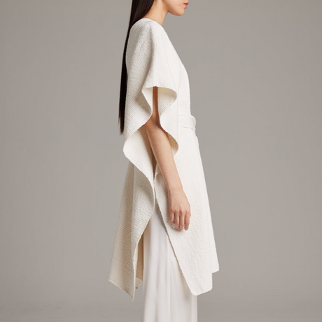 Woman wearing a white knit poncho against a gray background