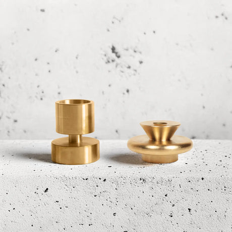 Two gold candle holders on a textured white surface with a light gray background